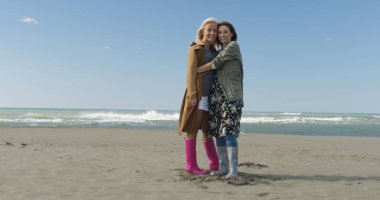 gülümseyen ve hayatın tadını çıkarırken sonbaharda iki sevimli genç kadın ışığında okyanus boyunca yürümek