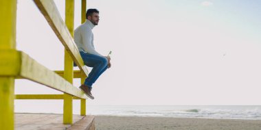 Sonbahar zamanı sahilde bira içen adam