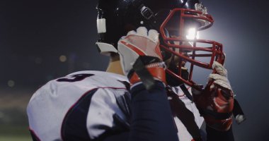 American football player putting on his protective helmet against bright stadium illumination lights clipart