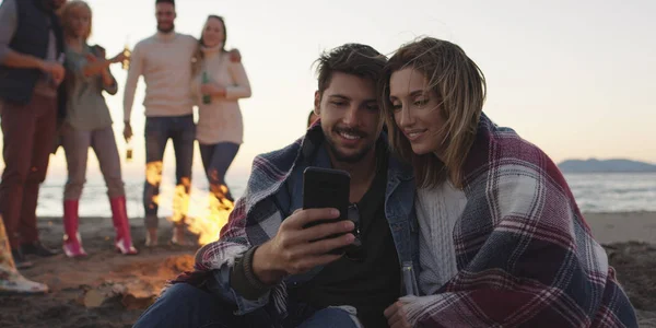 Paar Met Behulp Van Mobiele Telefoon Tijdens Strandfeest Met Vrienden — Stockfoto