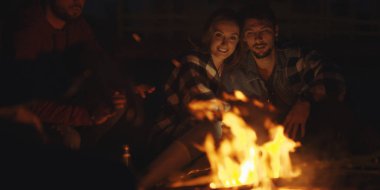 Genç bir çift, arkadaşlarıyla birlikte gece kumsalda oturup bira içiyor.