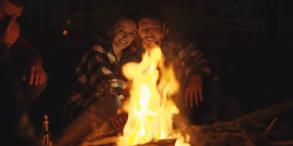 Young Couple Sitting with friends Around Campfire on The Beach At Night drinking beer