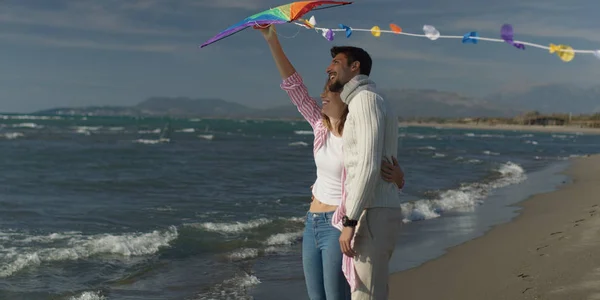 Счастливая пара веселится с воздушным змеем на пляже — стоковое фото