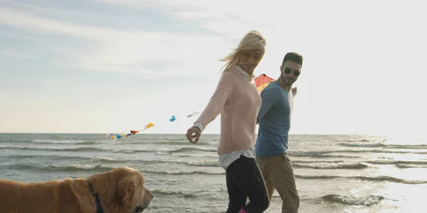 Pareja con perro divirtiéndose en la playa en día autmun —  Fotos de Stock