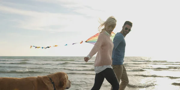 Para z psem zabawy na plaży na autmun dzień — Zdjęcie stockowe