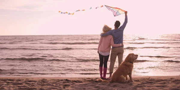 Пара с собакой веселятся на пляже в день осени — стоковое фото
