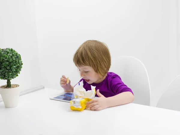 可爱的小女孩吃饼干 而在平板电脑上玩游戏在家里 — 图库照片