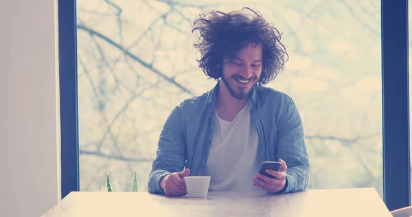 Schöner Junger Mann Trinkt Kaffee Und Benutzt Hause Ein Mobiltelefon — Stockfoto