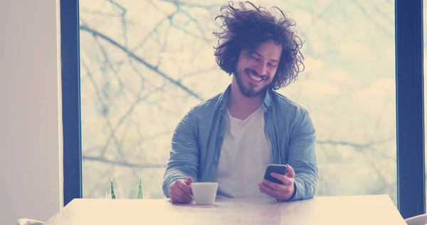 Schöner Junger Mann Trinkt Kaffee Und Benutzt Hause Ein Mobiltelefon — Stockfoto