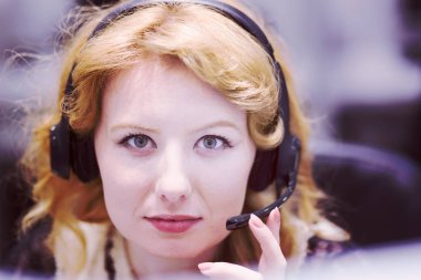 Genç, gülümseyen bir kadın çağrı merkezi operatörü kulaklıkla işini yapıyor.