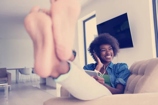 Mujer afroamericana en casa en silla con tableta y cabeza pho —  Fotos de Stock