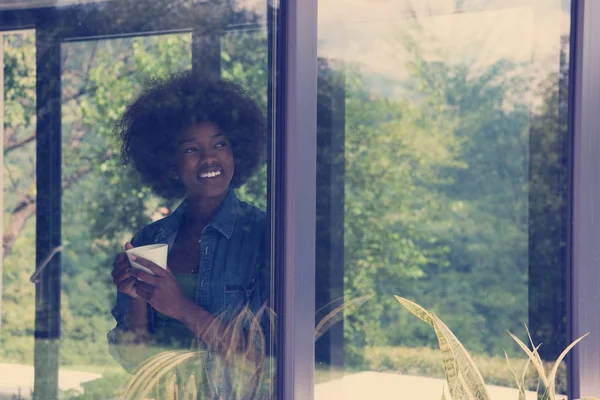 Mujer afroamericana bebiendo café mirando por la ventana —  Fotos de Stock