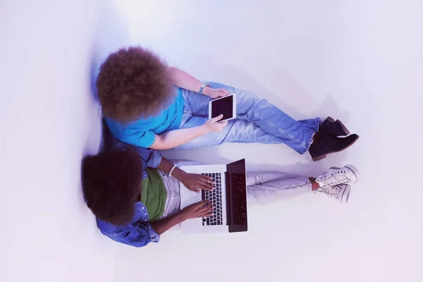 Multi-etnisch paar zittend op de vloer met een laptop en tablet — Stockfoto