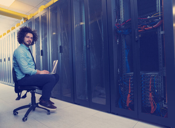 Мужчина IT-инженер, работающий на ноутбуке в серверной в современном дата-центре