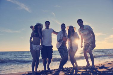 Mutlu genç arkadaş grubu gün batımında sahilde zıplarken ve koşarken eğleniyor ve kutluyor.