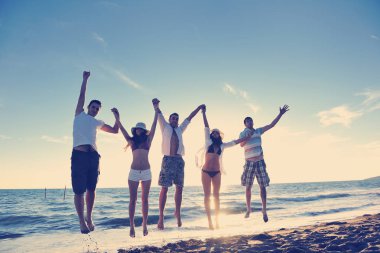 Mutlu genç arkadaş grubu gün batımında sahilde zıplarken ve koşarken eğleniyor ve kutluyor.