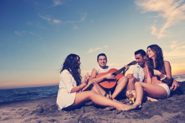 Mutlu genç arkadaş grubu gün batımında sahilde zıplarken ve koşarken eğleniyor ve kutluyor.