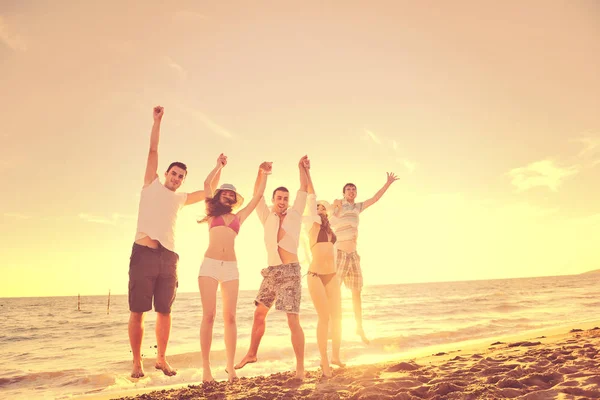 Mutlu genç arkadaş grubu gün batımında sahilde zıplarken ve koşarken eğleniyor ve kutluyor.