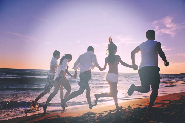 在日落时分 快乐的年轻人群在海滩上欢快地奔跑和跳跃 — 图库照片