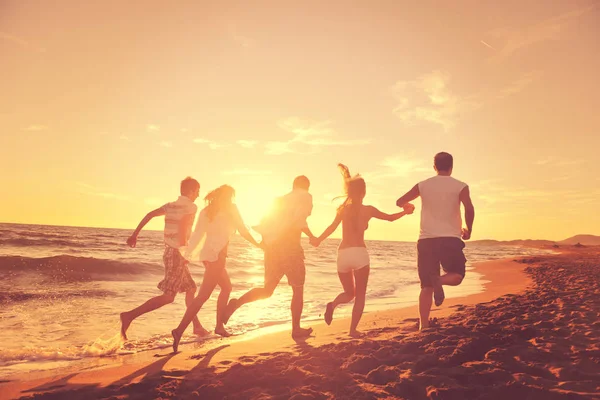 幸せな若者グループは白いランニングを楽しみながら日没時にビーチをジャンプします — ストック写真