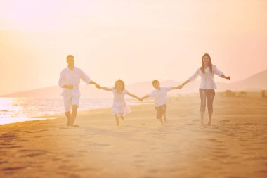 Mutlu genç aile gün batımında sahilde eğleniyor.