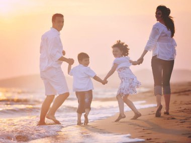 Mutlu genç aile gün batımında sahilde eğleniyor.