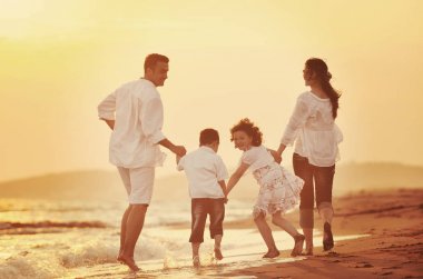 Mutlu genç aile gün batımında sahilde eğleniyor.