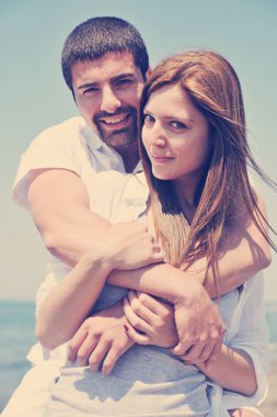 Mutlu genç çiftler yaz mevsiminde sahilde eğlenceli ve romantik anlar yaşarlar ve mutluluk ve seyahat kavramını temsil ederler.