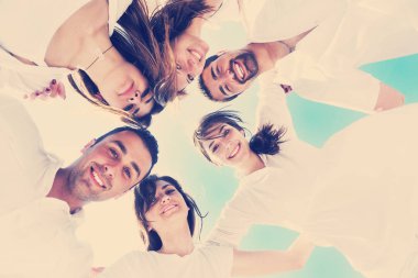Kumsalda bir grup mutlu genç eğleniyor ve gülümsüyor.