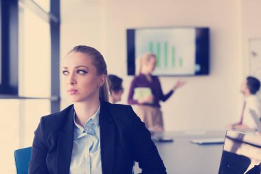Modern ofis içinde genç iş kadınının portresi, arka planda toplantı grubu.