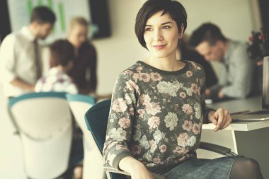 Modern ofis içinde genç iş kadınının portresi, arka planda toplantı grubu.