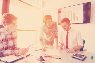 Girişimci genç yaratıcı insanlar grup fikir planlarını not etmek için dizüstü bilgisayar ve tablet bilgisayar kullanarak toplantı üzerinde beyin fırtınası yapıyorlar ve gündoğumu ya da günbatımı projelerini arka planda güneş ışığıyla birlikte kaydediyorlar.