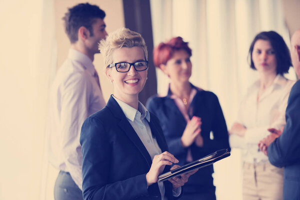 Smilling senior older  business woman with tablet computer  in front her team blured in background. Group of young business people at modern bright  startup office interior.