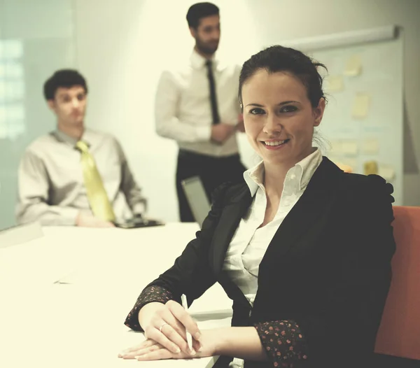 young business woman on meeting usineg laptop computer, blured group of people in background at  modern bright startup office interior taking notes on white flip board and brainstorming about plans and ideas