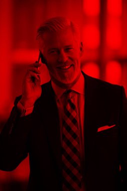 Modern aydınlık ofis içlerinde kıdemli iş adamı cep telefonuyla konuşur.