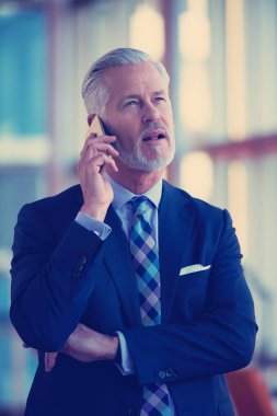 Modern aydınlık ofis içlerinde kıdemli iş adamı cep telefonuyla konuşur.
