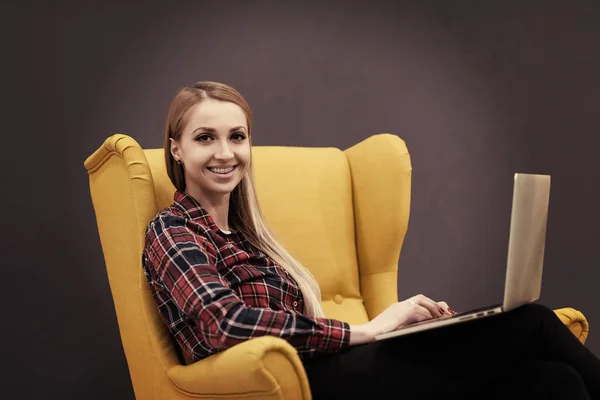 スタートアップビジネス現代オフィスのラップトップコンピュータで働く女性創造的な黄色のアームチェアに座って — ストック写真