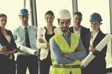 İş adamları, inşaat mühendisi mimar ve işçi görünümlü yapı modeli ve proje planlarıyla modern ofiste toplantı ve sunum üzerine bir araya geldiler.