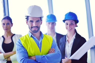 İş adamları, inşaat mühendisi mimar ve işçi görünümlü yapı modeli ve proje planlarıyla modern ofiste toplantı ve sunum üzerine bir araya geldiler.