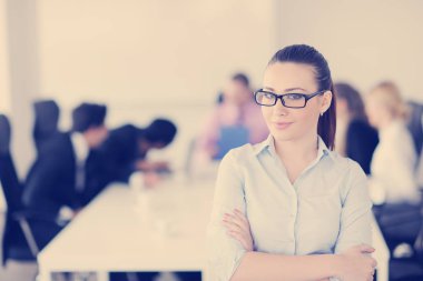 Başarılı bir iş kadını, modern parlak ofiste çalışanlarıyla arka planda duruyor.