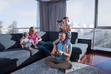 Mutlu bir aile. Baba, anne ve çocuklar video oyunu oynuyorlar. Baba ve oğul yerde oyun oynuyorlar.