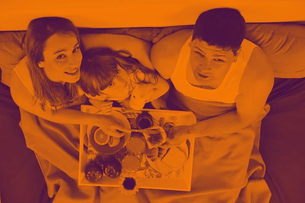 Szczęśliwy młody rodzina jeść śniadanie w łóżku — Zdjęcie stockowe