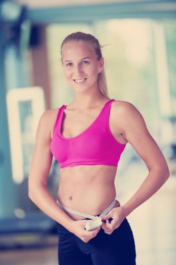 Formda genç bir kadın spor salonunda karnını ölçüyor.
