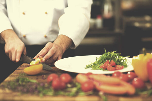 Chef serving vegetable salad on plate in restaurant kitchen