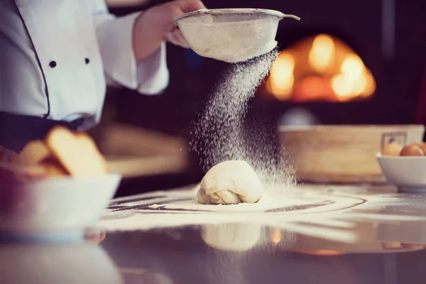 Szef kuchni posypywanie mąki na świeże ciasto pizzy — Zdjęcie stockowe