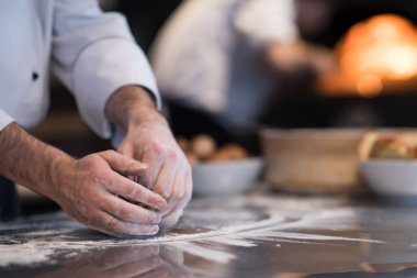 Şef elleri pizza için hamur hazırlarken masaya un serpiştirmiş.