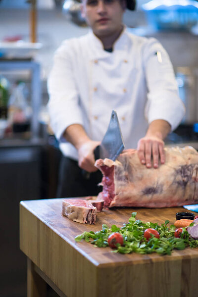 chef using ax while cutting big piece of beef  on wooden board in restaurant kitchen