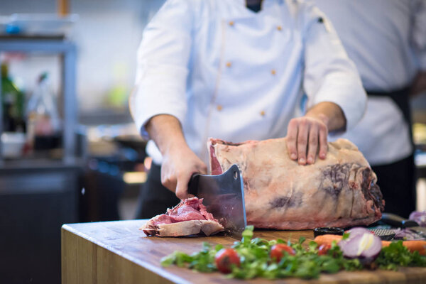 chef using ax while cutting big piece of beef on wooden board in restaurant kitchen