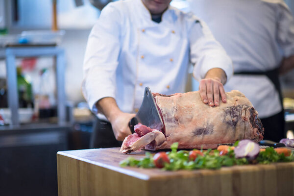chef using ax while cutting big piece of beef  on wooden board in restaurant kitchen