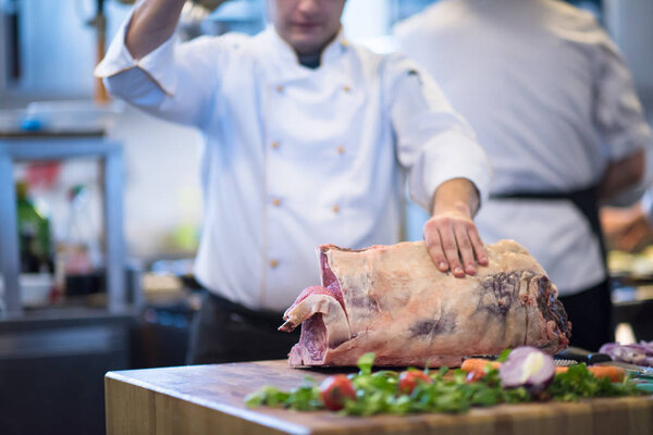 chef using ax while cutting big piece of beef  on wooden board in restaurant kitchen